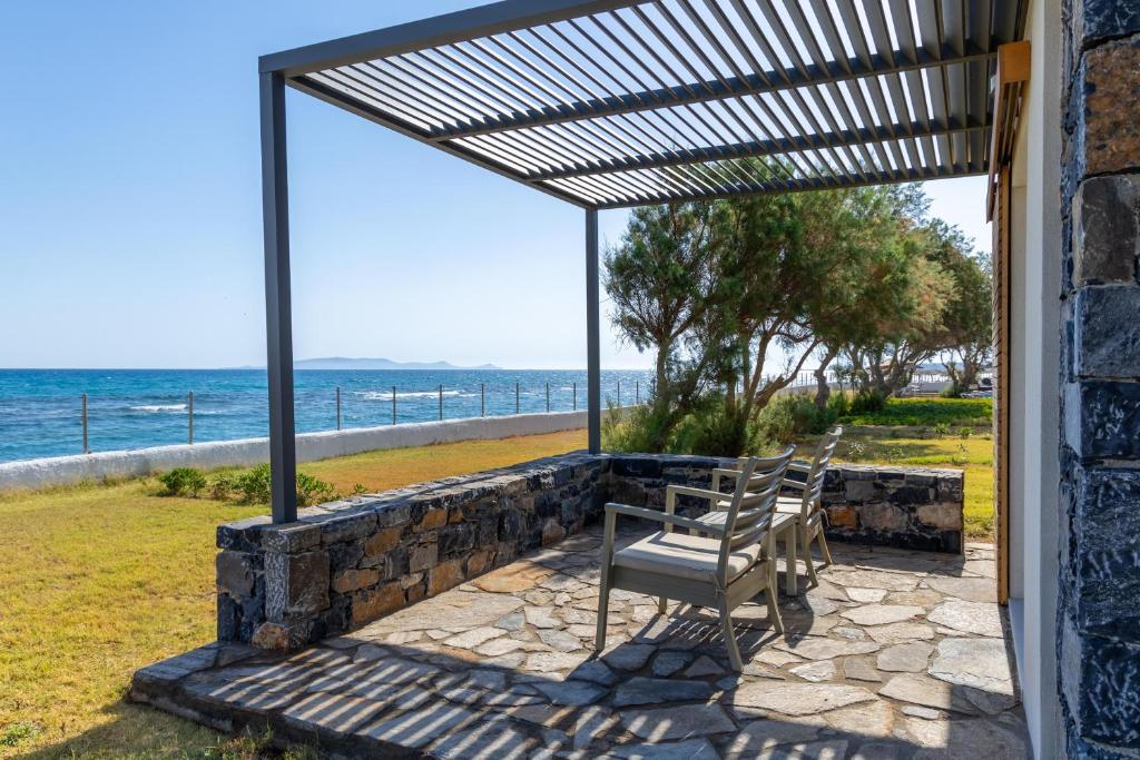 Jūras krastā izvietots terases stūrītis ar akmens grīdu un ērtām krēslām, kas nodrošina mierīgu vietu atpūtai un skatu uz zilo ūdeni.