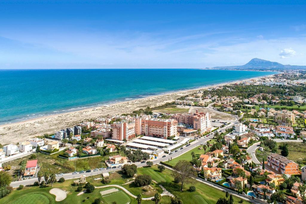 Jūras piekrastes ainava ar modernām viesnīcām un dzīvojamo apbūvi, kas izklāta gar smilšainām pludmalēm un zilām ūdenīm. Tālumā redzams kalns un attīstīta infrastruktūra, kas piedāvā brīvdienu iespējas.