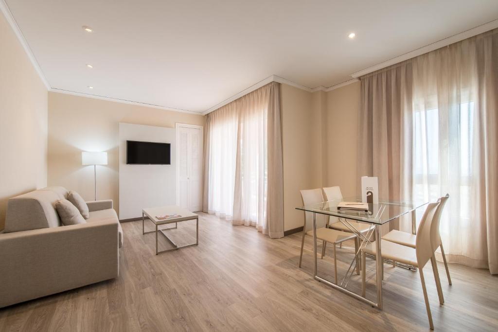 Mūsdienīgs viesistabas interjers ar ērtu dīvānu, gludu stikla galdu un gaišām aizkariem, kas ļauj ienākt dabiskajai gaismai. Ideāls telpa relaksācijai un ērtai atpūtai.