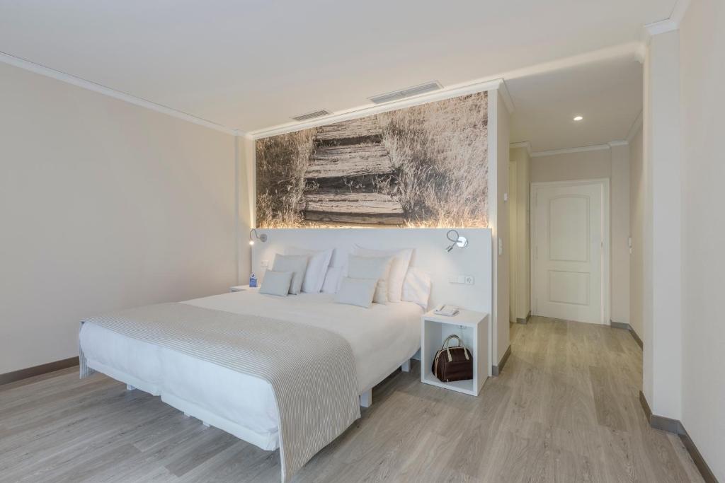 Mūsdienīga guļamistaba ar ērtu gultu, minimālistisku dizainu un dabas ainavas fotogrāfiju uz sienas, kas rada mierīgu atmosfēru. Guļamistabā ir arī naktsgaldiņš un gaismas avoti.