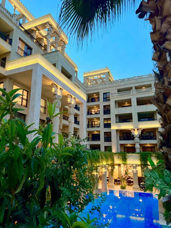 Eleganta viesnīca ar baseinu un zaļu dārzu, iedegusies vakara gaismā. Modernā arhitektūra un greznas detaļas veido patīkamu atmosfēru.