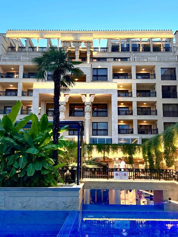 Eleganta viesnīca ar palmām un greznu arhitektūru, kas atrodas blakus baseinam. Vakarā apgaismojums izceļ ēkas detaļas un viesnīcas apkārtni.