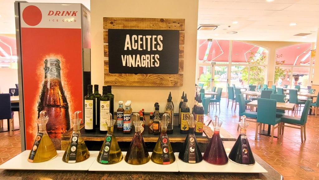 Eļļu un etiķu stends ar dažādām pudelēm, kas izvietotas uz galda, un restorāna interjers fona.