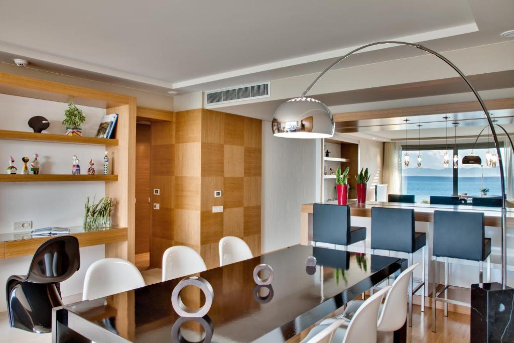 Mūsdienīgs dzīvojamās telpas interjers ar ēdamgaldu, melno koka virsmu un stilīgu lampu, kas izgaismo telpu. Logā redzams gleznains skats uz jūru.