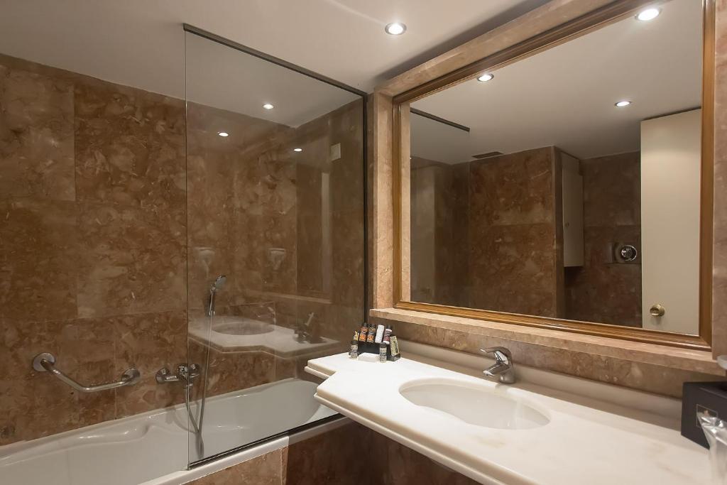 Mūsdienīgs vannas istabas dizains ar marmora akcentiem, stikla dušas kabīni un elegantu spoguli. Vanna un izlietne nodrošina komfortu un stilīgu izskatu.