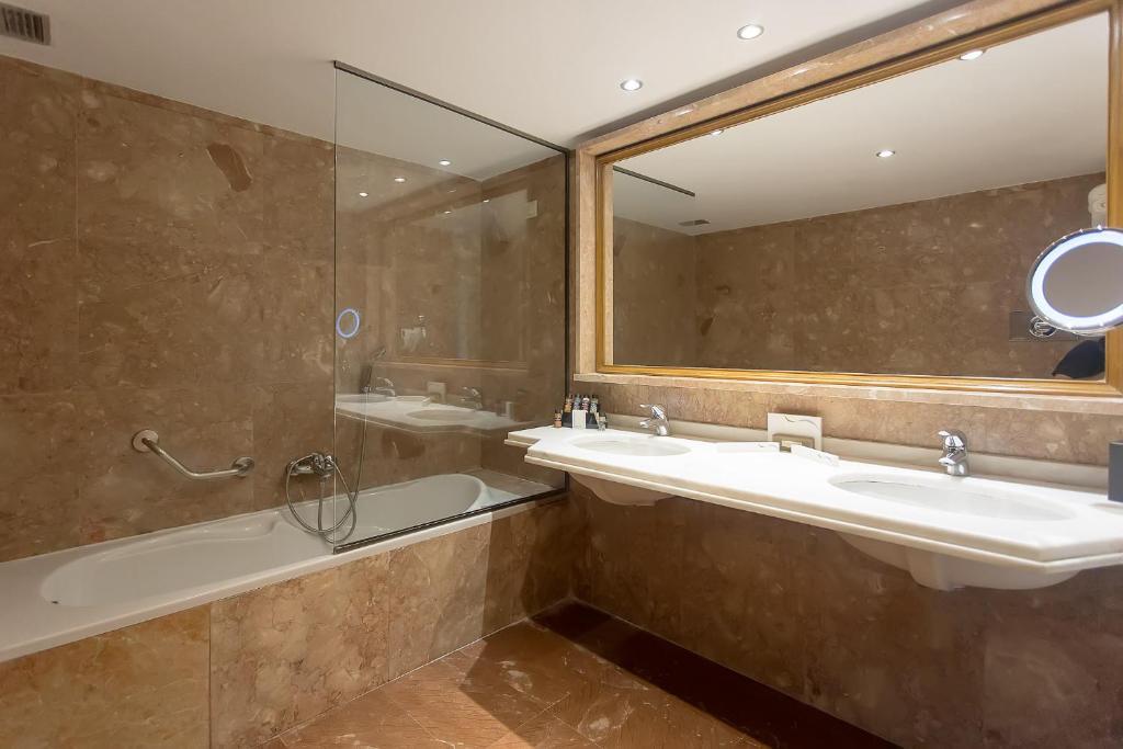 Mūsdienīgs vannas istabas interjers ar akmens sienām, dušas kabīni un divām izlietnēm. Gaismas spogulis un vannas istabas piederumi pievērš uzmanību.