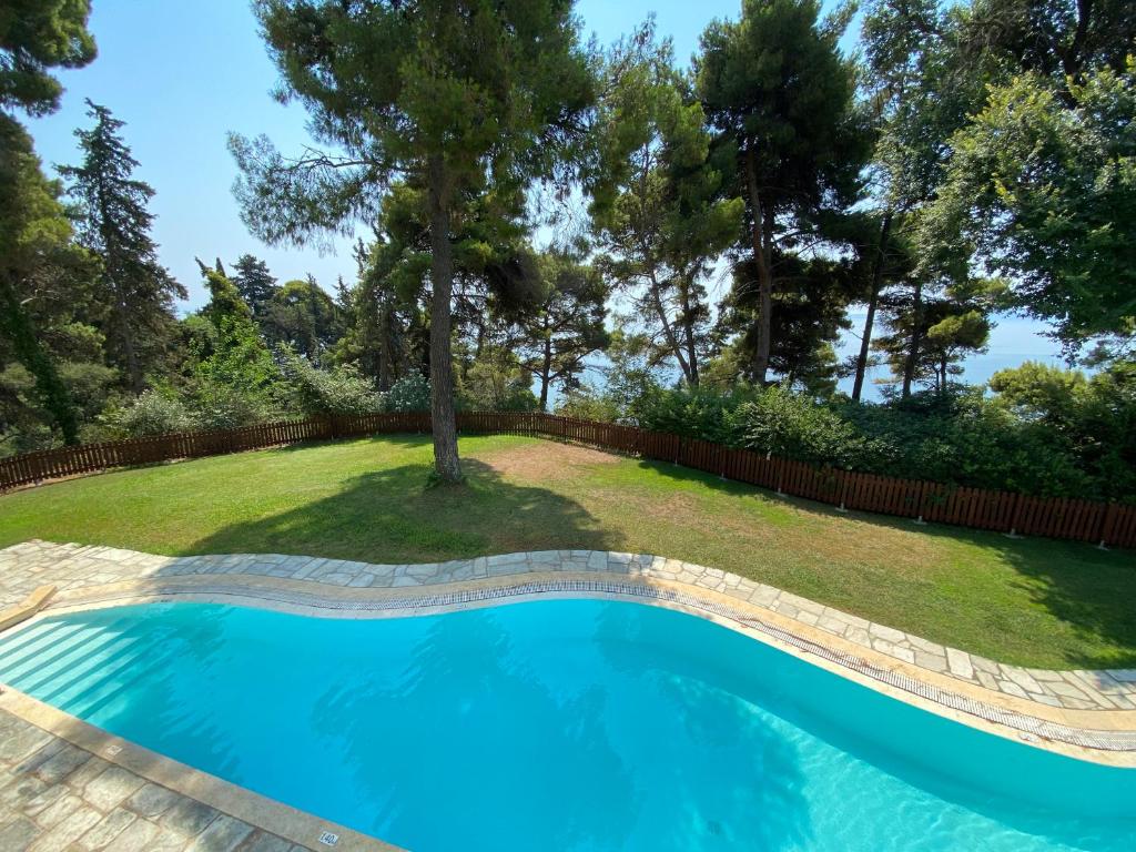 Peldbaseins ar dzidru ūdeni, ko ieskauj zaļš zāliens un koku rinda, nodrošina mierīgu atpūtas vietu. Fons ar jūras skatu papildina ainavu.