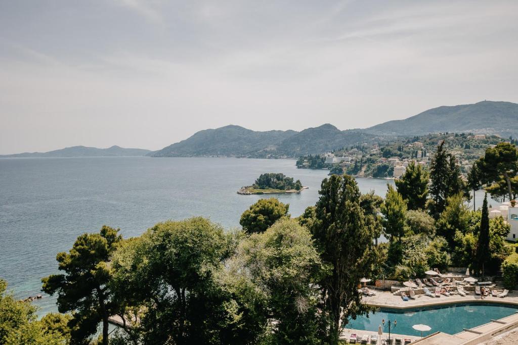 Skats uz jūru ar kalniem un saliņu, ko ieskauj zaļumi un peldbaseins. Ideāla vieta atpūtai un dabas baudīšanai.