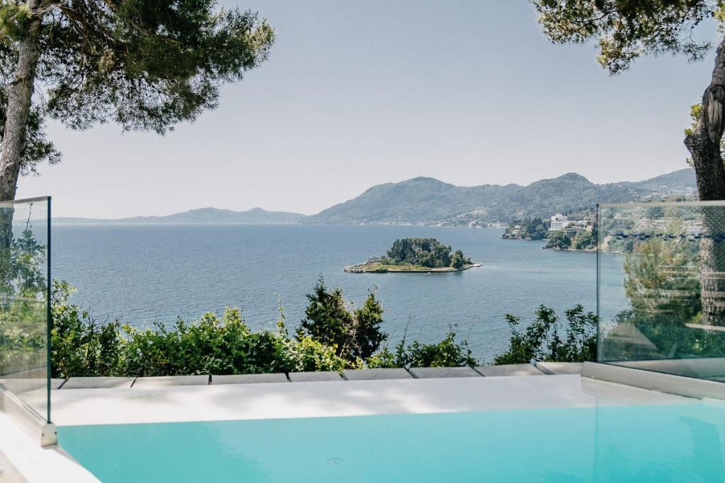 Skats uz jūru ar nelielu salu un kalnu fona, no mūsdienīgas mājas terases ar baseinu.