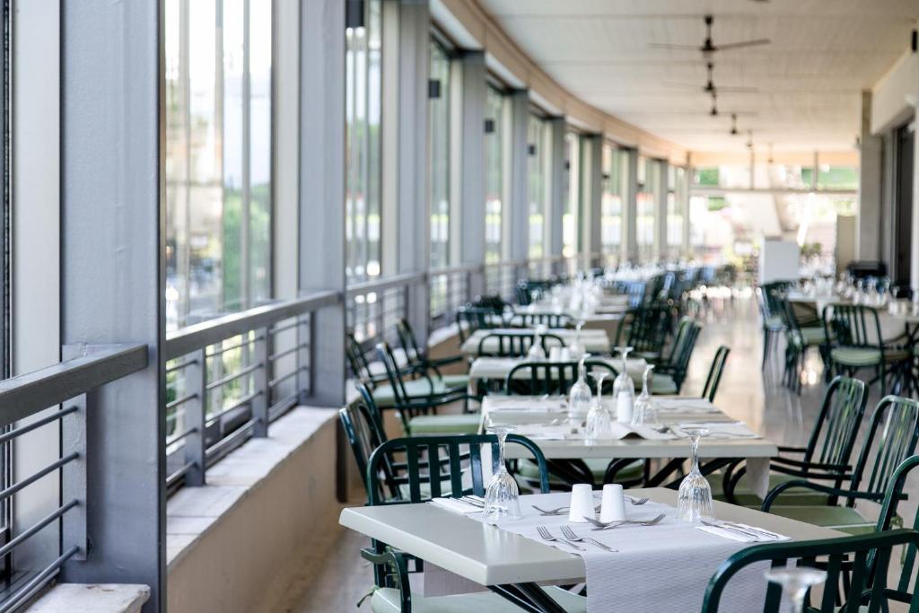 Gaišs restorāns ar lieliem logiem, kas piedāvā skatu uz āru. Galdi ir klāti ar baltiem galdautiem un glāzēm, radot elegantu atmosfēru.