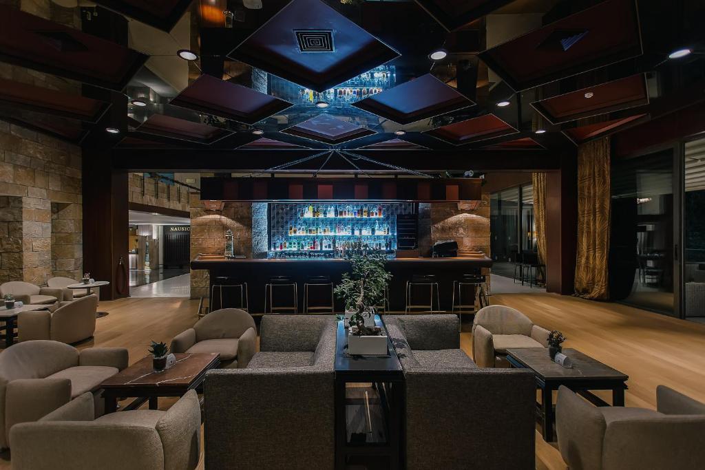 Mūsdienīgs bārs ar elegantiem mīkstajiem krēsliem un stilīgu apgaismojumu, kurā redzama dzērienu plauktu siena. Interjers apvieno akmens un koka elementus, radot siltu un viesmīlīgu atmosfēru.