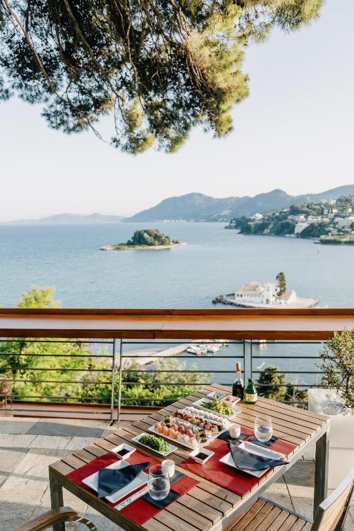 Skats uz jūru no terases ar galdu, kas klāts ar sushi un dzērieniem, radot relaksējošu atmosfēru. Apkārt esošā ainava papildina brīvdienu sajūtu.