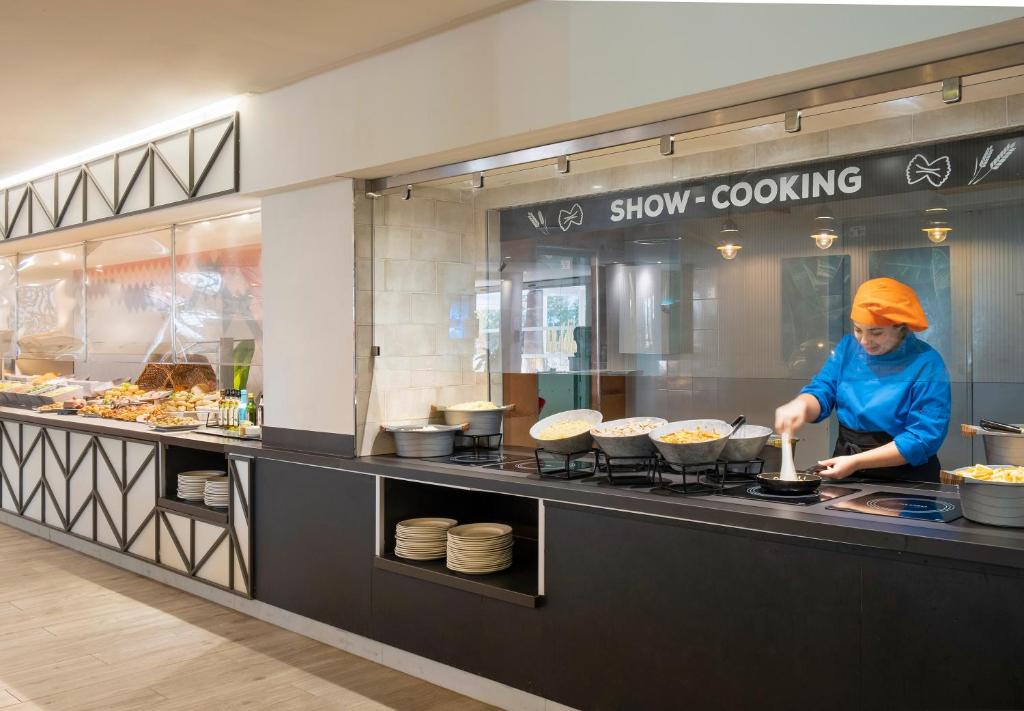 Šajā ēdināšanas zonā redzams pavārs, kas gatavo ēdienus pie "SHOW-COOKING" stenda, kurā ir dažādi ēdieni un sastāvdaļas. Moderns interjers un dinamiska atmosfēra rada lielisku pieredzi viesiem.