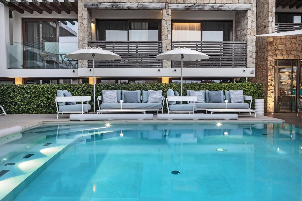 Mūsdienīgas atpūtas zonas pie baseina ar ērtām dīvānu vietām un saulessargiem, apkārtne ar zaļām dzīvžogiem.