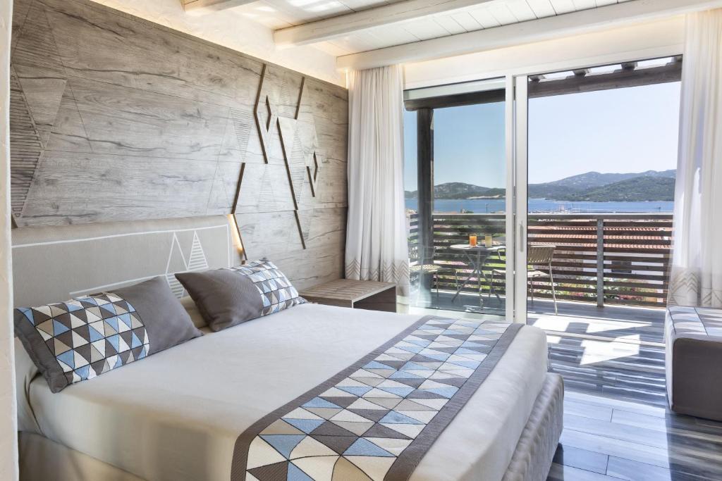 Mūsdienīgs guļamistabas interjers ar koka sienu un skatu uz jūru. Gultā ir dekoratīvi spilveni ar ģeometriskiem rakstiem.