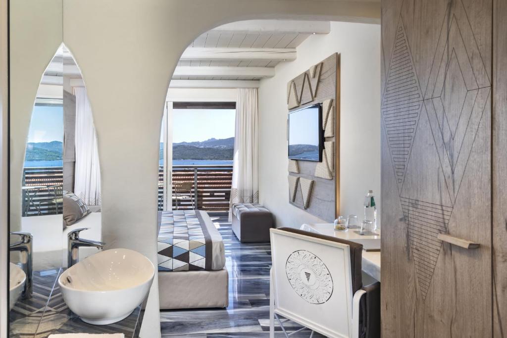 Mūsdienīgs viesnīcas numurs ar elegantu interjeru un panorāmas skatu uz kalniem. Telpa ietver stilīgu gultu, televizoru un atpūtas stūri ar rakstainu grīdu.