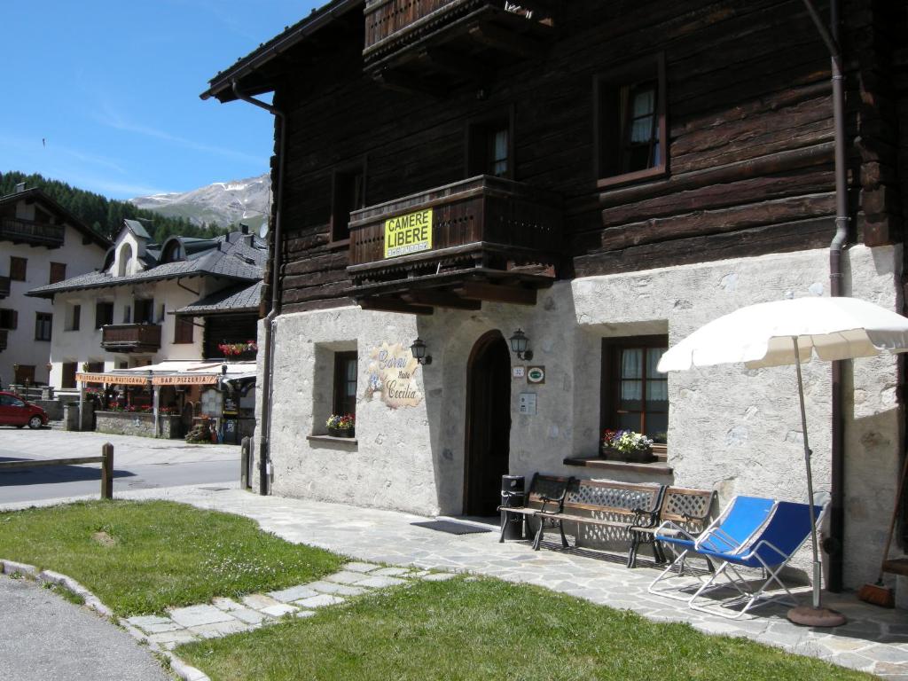 Tradicionāla kalnu māja ar koka fasādi, kurā ir pieejamas brīvas istabas. Priekšā atrodas soli un saulessargs, apkārt skaista ainava ar kalniem.