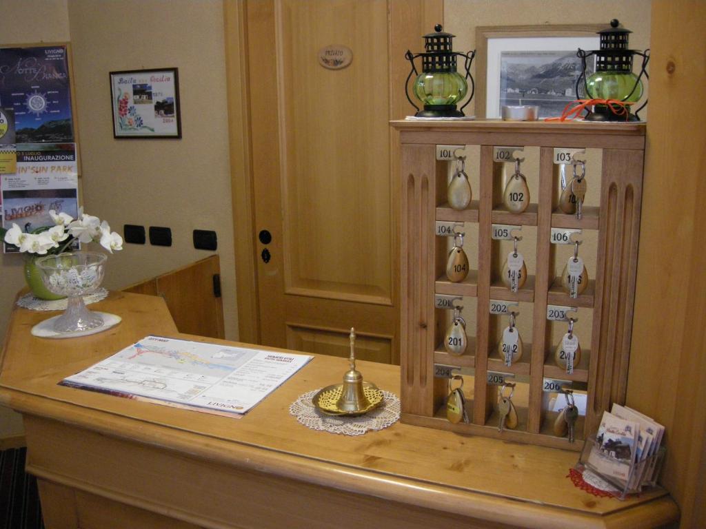 Reģistratūras zona ar koka galdu, uz kura atrodas viesnīcas numuru atslēgas un informācijas brošūras, kā arī dekoratīvas lampas un ziedu kompozīcija.