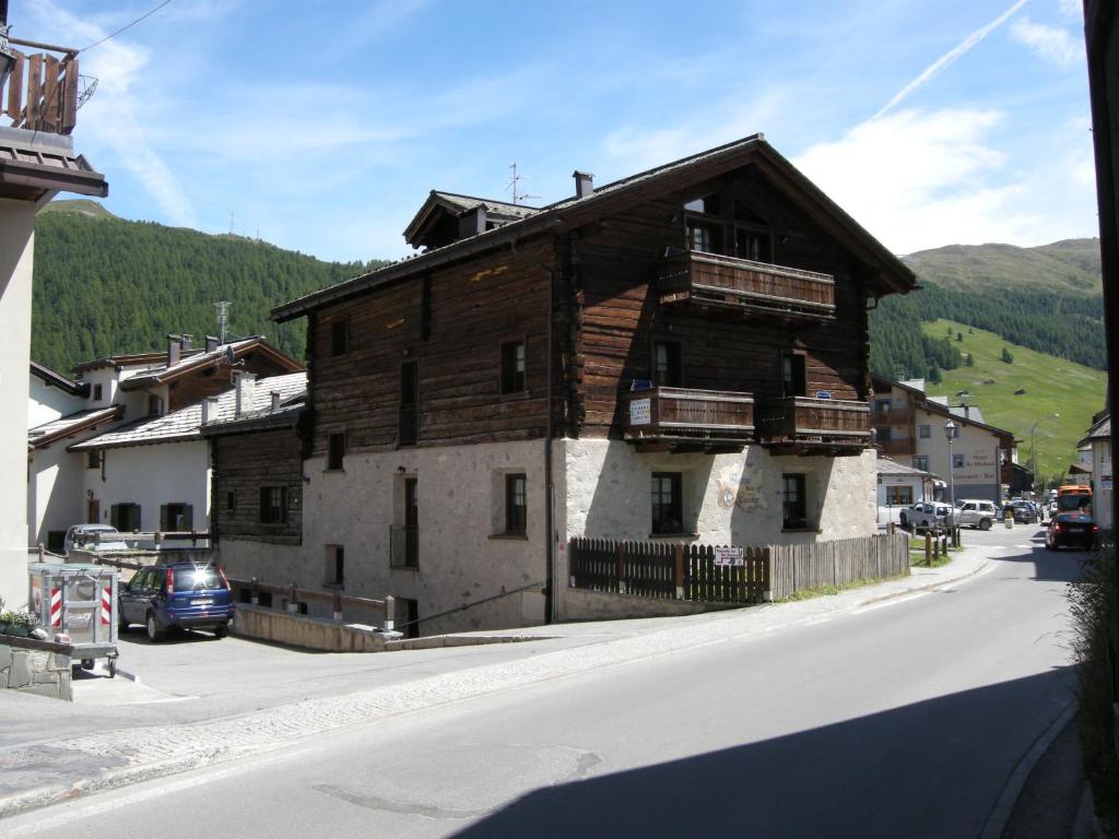 Mājas ar koka un akmens fasādi kalnu apkārtnē, redzamas balkoni un asfaltēta iela. Apkārtnē ir zaļi pakalni un citi mājokļi.