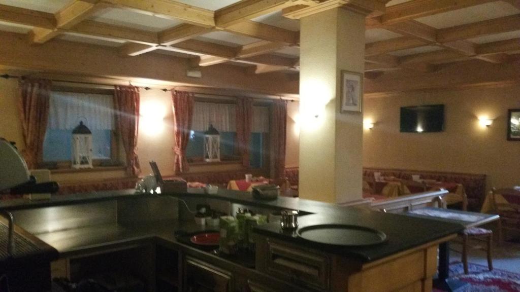 Mūsdienīga restorāna iekārtojums ar koka griestiem un siltu apgaismojumu, kurā redzama bāra zona un ēdamzona ar galdiem un krēsliem.