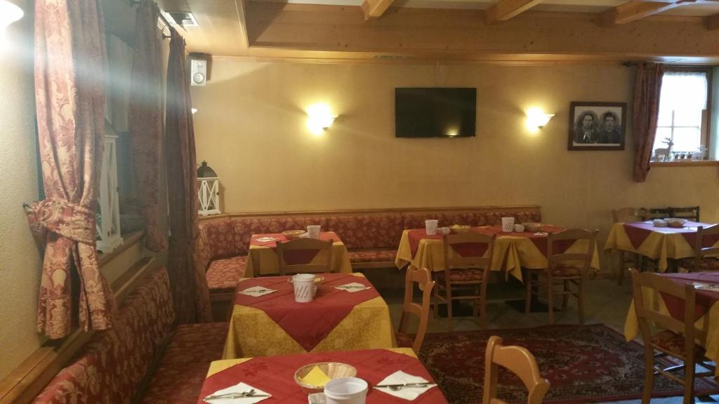 Restorāna interjers ar sarkanām un dzeltenām galdautām, koka mēbelēm un siltiem apgaismojumiem, radot mājīgu atmosfēru. Uz sienas redzams televizors un dažas dekoratīvas gleznas.