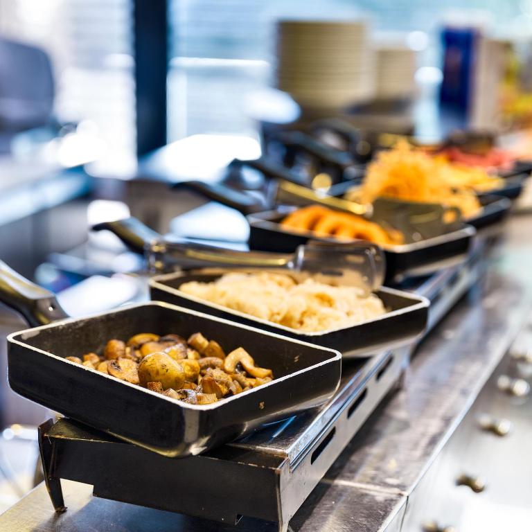 Brokastu bufete ar dažādiem ēdieniem, tostarp dārzeņiem un kartupeļiem, pasniegta melnās pannās.