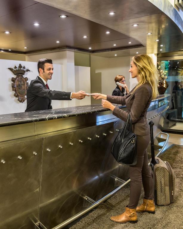 Recepcijas darbinieks pasniedz dokumentu viesim, kurš stāv pie viesnīcas reģistratūras. Viesis izskatās apmierināts un gatavs pārbaudīt.