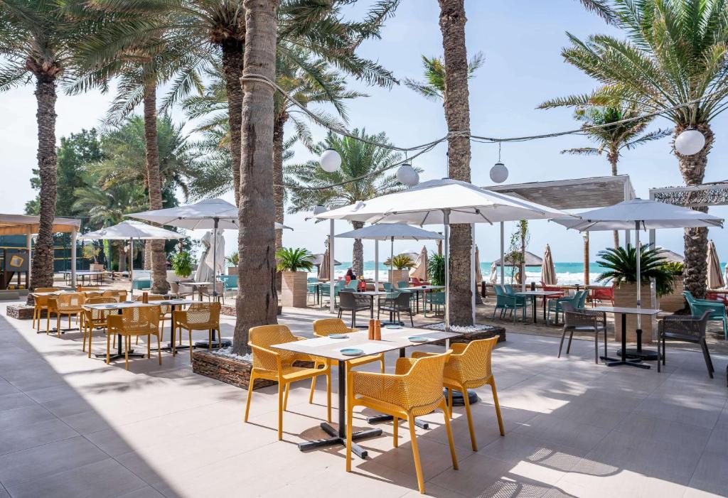 Āra restorāna zona ar palmām, saulessargiem un krēsliem, kas piedāvā relaksējošu atmosfēru pie jūras. Ideāla vieta ēdienu baudīšanai un atpūtai.