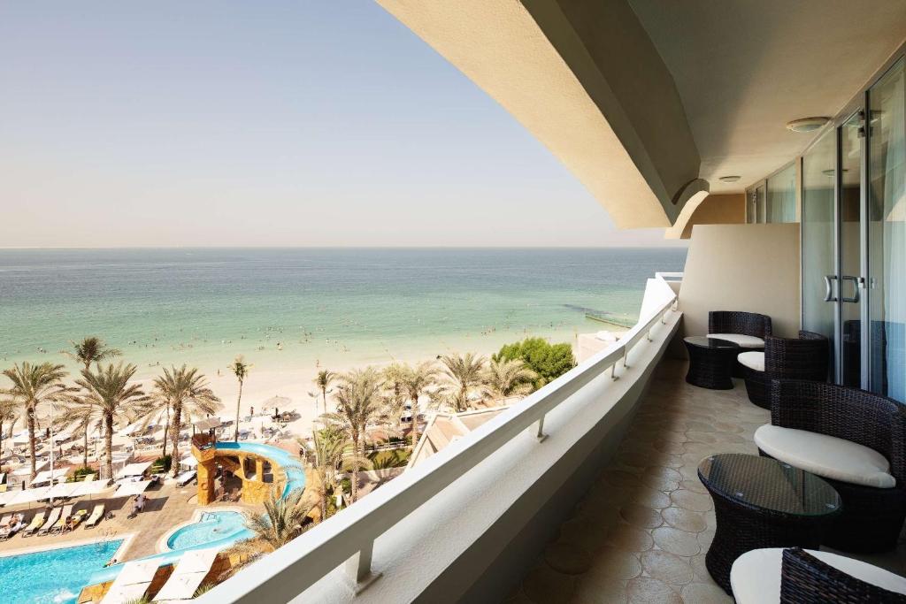 Balcony view over a serene beach with crystal-clear water, palm trees, and a swimming pool. Ideal for relaxation and enjoying the coastal scenery.