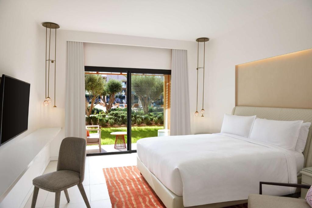 Mūsdienīgs viesnīcas numurs ar lielu logu un skatu uz dārzu, iekārtots ar ērtu gultu un stilīgu interjeru. Šajā telpā ir televizors un eleganta mēbele, radot relaksējošu atmosfēru.