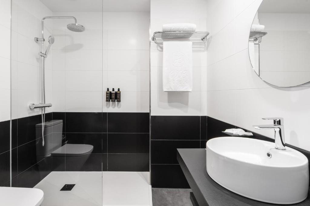Mūsdienīgs vannas istabas interjers ar melnā un baltā krāsā, ietver dušu, tualeti un izlietni. Iekārtots ar stilīgu spoguli un higiēnas piederumiem.