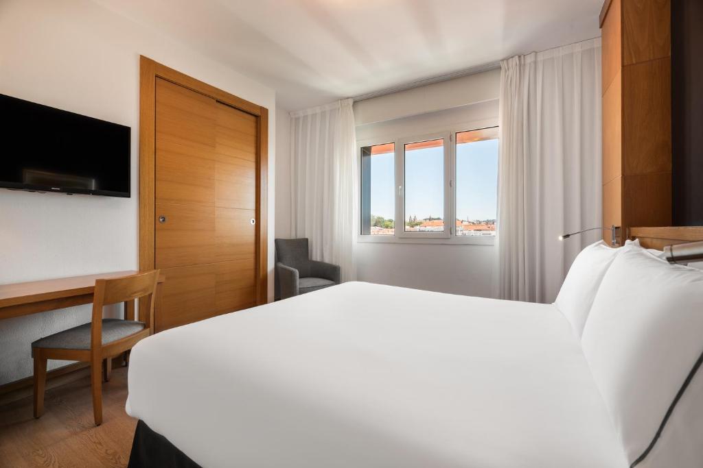 Mūsdienīga viesnīcas numuriņa interjers ar gultu, rakstāmgaldu un televizoru. Logi piedāvā skatu uz ārpusi, radot gaišu un gaisīgu atmosfēru.