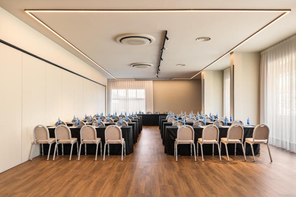Konferences zāle ar melniem galdautiem, organizēta ar krēsliem un ūdens pudelēm, gaiša un moderna vide.