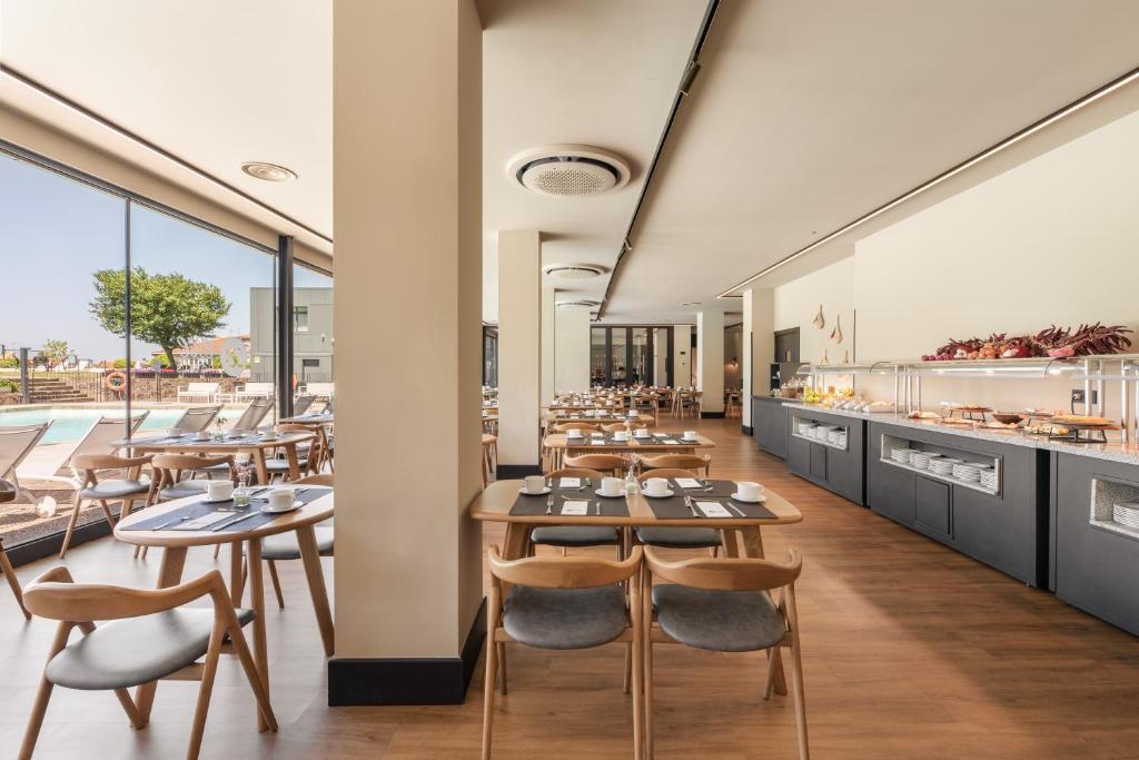 Moderns restorāns ar plašām logiem, kas piedāvā skatu uz baseinu. Interjerā ir koka mēbeles un bufete ar dažādiem ēdieniem.