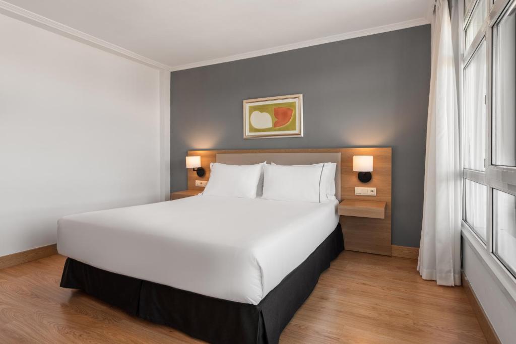 Mūsdienīgs guļamistabas interjers ar plašu gultu, koka grīdu un neitrālām krāsām. Sienā redzama mākslas gleznas kompozīcija, radot patīkamu atmosfēru.