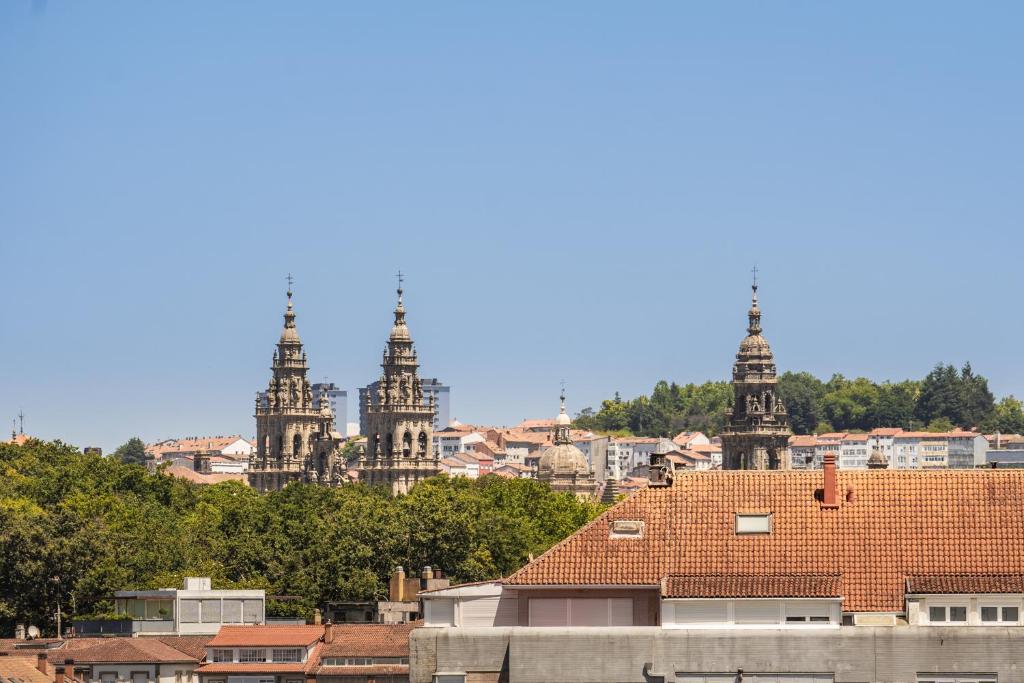 Skats uz trīs vēsturiskām baznīcas torņiem, kas izceļas pār pilsētas ainavu ar zaļām koku rindām un jumtiem.