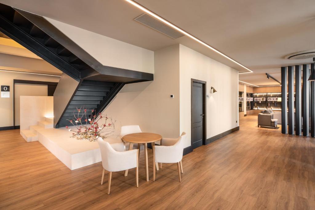 Mūsdienīga interjera telpa ar melnu kāpņu konstrukciju, koka grīdu un elegantu galdu ar krēsliem. Dabiska apgaismojuma un izsmalcinātu dekoru kombinācija rada siltu atmosfēru.