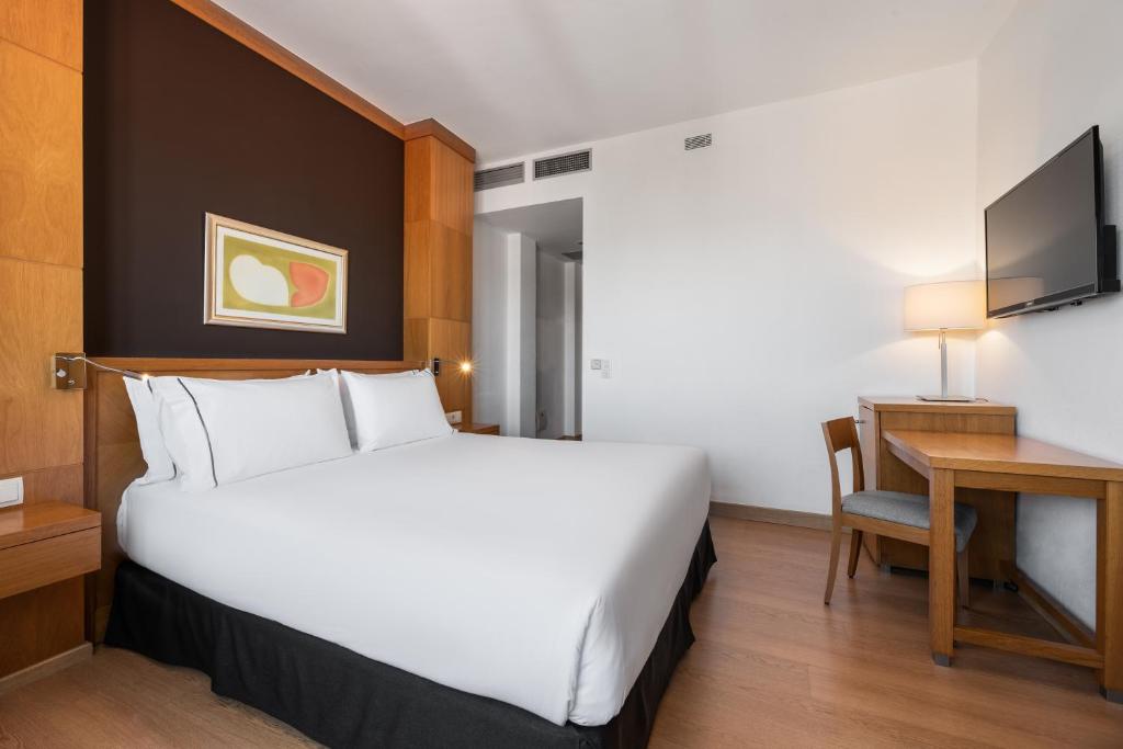 Mūsdienīga viesnīcas numura iekārtojums ar plašu gultu, koka elementiem un darba galdu, papildināts ar televizoru un gaismas avotu.