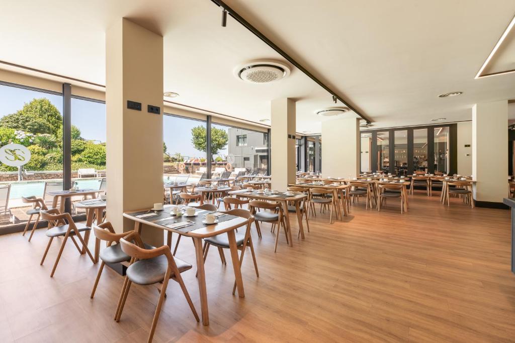 Moderns restorāns ar koka grīdu un gaišām logu sienām, kas piedāvā skatu uz ārējiem dārziem un baseinu. Galdi ir sakārtoti ar krēsliem, radot ērtu un viesmīlīgu atmosfēru.