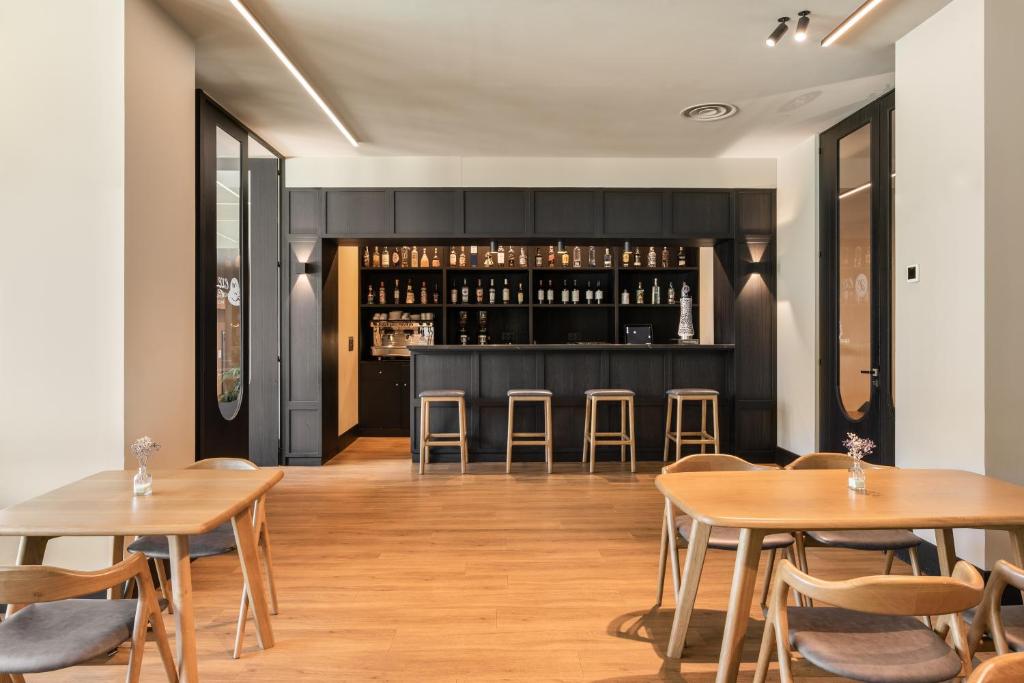 Mūsdienīgs bārs ar tumšu koka interjeru un koka galdiem, kas veidots relaksējošai atmosfērai. Uz bāra plaukta redzami dažādi dzērieni un kafijas automāts.