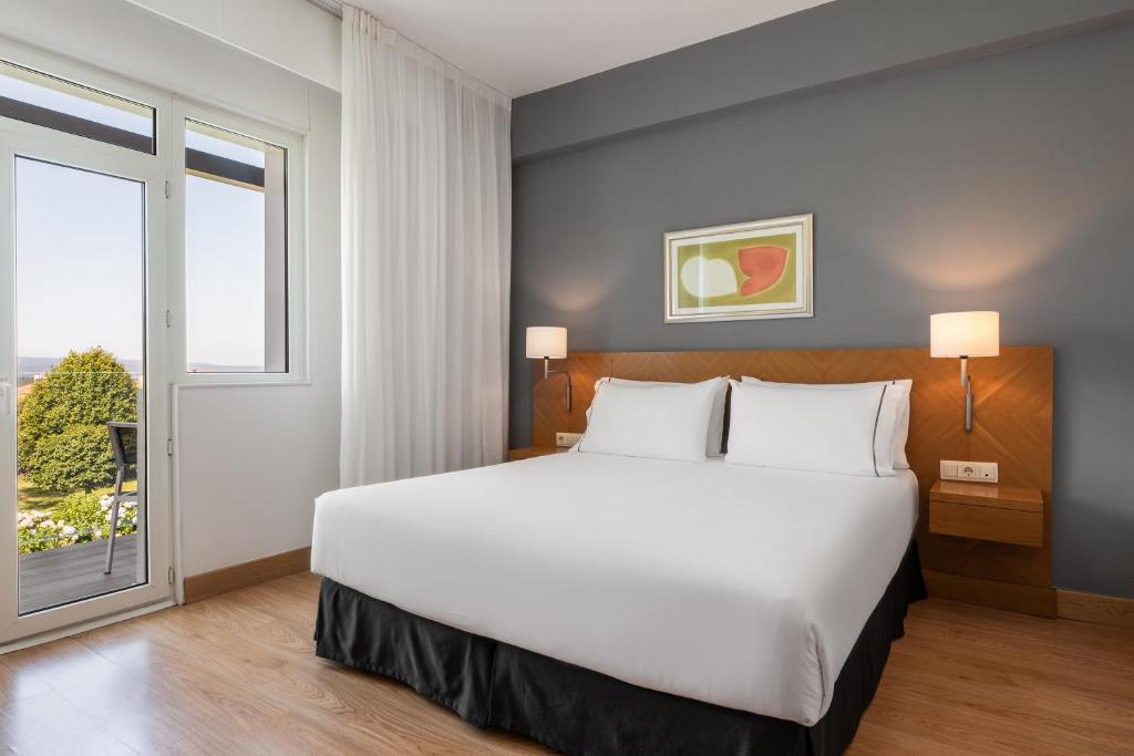 Moderns viesnīcas numurs ar plašu gultu, gaišām krāsām un logiem, caur kuriem redzams dārzs. Iekārtojums ietver mākslas darbu uz sienas un naktslampas.