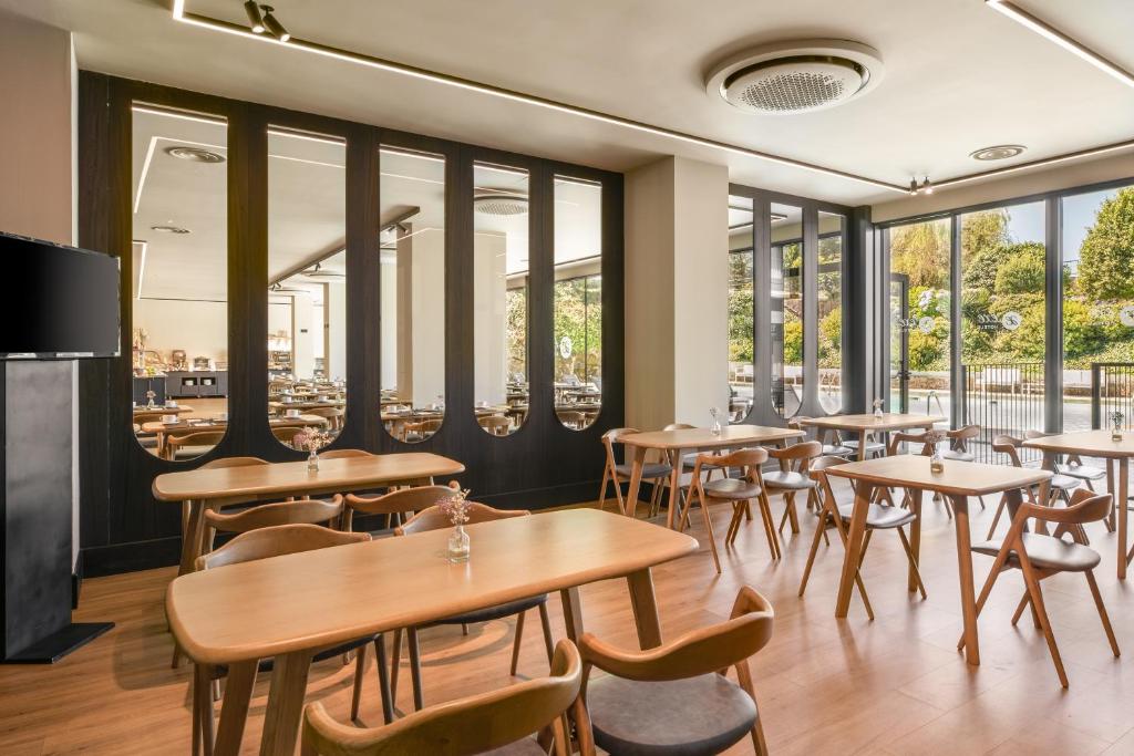 Mūsdienīgs kafejnīcas interjers ar koka galdiem un krēsliem, plašiem logiem un atspoguļojumiem. Gaisma rada patīkamu atmosfēru, kas aicina apmeklētājus atpūsties.