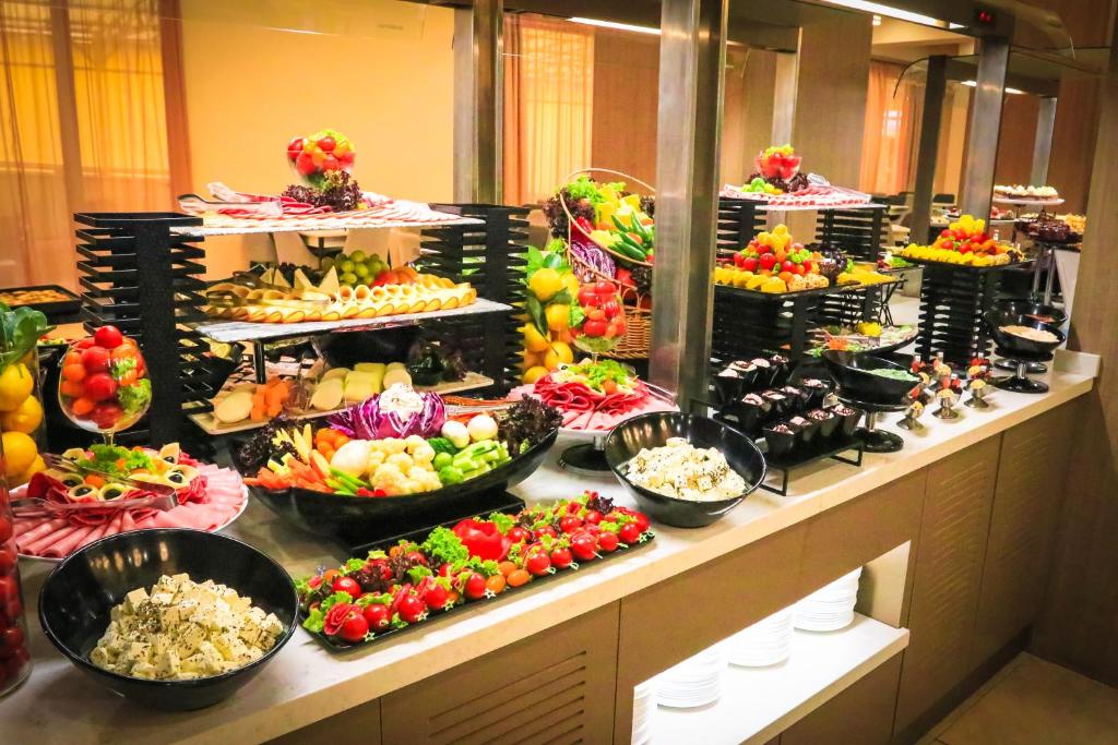 Svaigu augļu un dārzeņu bufete ar daudzveidīgām uzkodām, tostarp salātiem, gaļas plāksnēm un desertiem. Krāsaini un pievilcīgi izkārtoti ēdieni, kas aicina uz gardu maltīti.