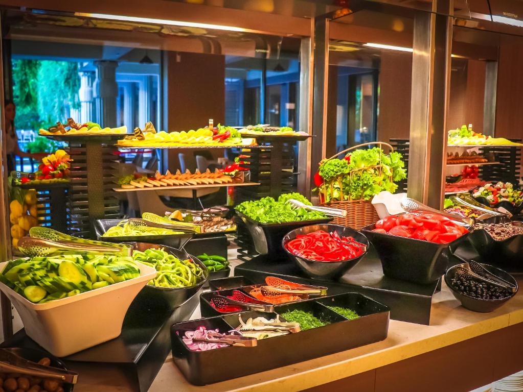 Svaigu dārzeņu bufete ar dažādām salātiem un garnējumiem, izkārtota pie elegantas viesnīcas. Piemērota veselīgas ēšanas izvēlēm.