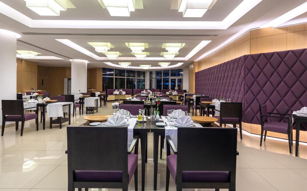 Mūsdienīga restorāna interjers ar elegantām galdiem un krēsliem, apgaismots ar modernām lampām. Svaigi ziedi uz galdiem piešķir atmosfēru.
