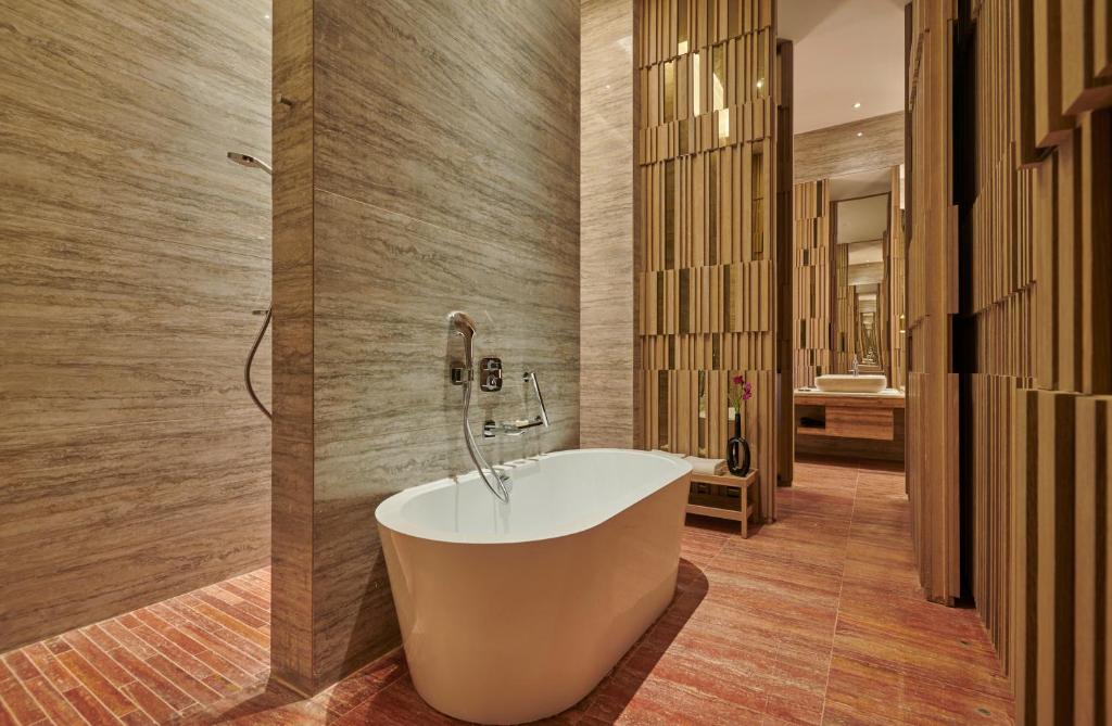 Mūsdienīgs vannas istabas interjers ar brīvo stāvošu vannu un koka akcentiem, kas rada relaksējošu atmosfēru. Sienas apdare un apgaismojums piešķir telpai eleganci.