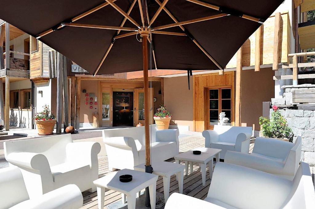 Āra atpūtas zona ar baltām mēbelēm un lielu, tumšu lietussargu, kas sniedz ēnu. Fons veidots no dabīgām koka un akmens detaļām, radot elegantu un relaksējošu atmosfēru.