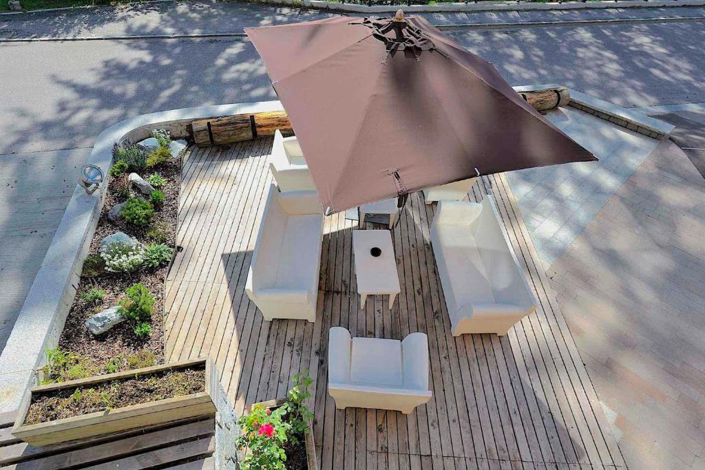 Āra terase ar baltiem dīvāniem, galdu un lielu brūnu saules jumtu, apkārt ziediem un augiem. Terase ir izgatavota no koka un ir labi apgaismota.