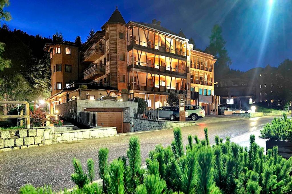 Nakts skats uz modernu viesnīcu kalnu apvidū, apgaismotu ar siltu gaismu, kas izceļ tās arhitektūru un apkārtni. 