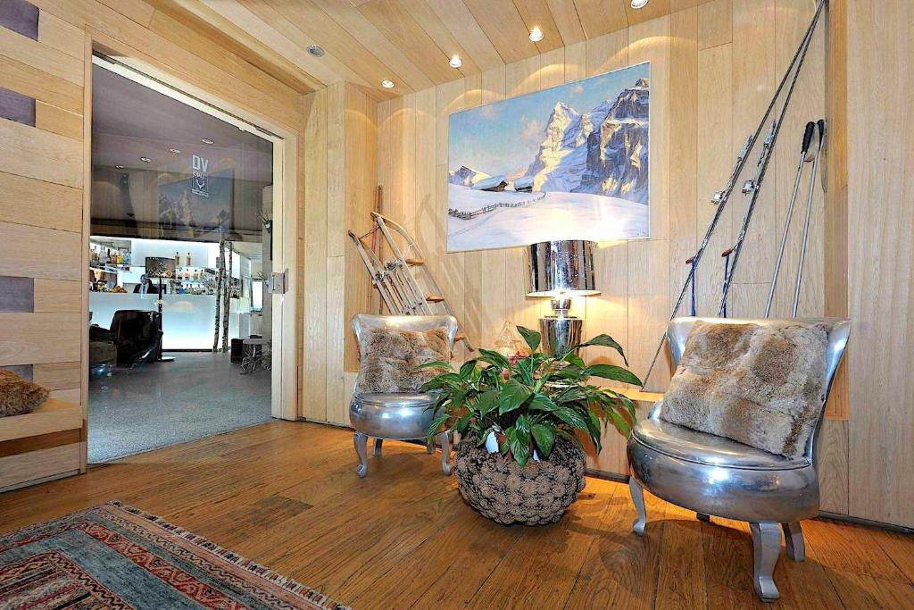 Moderns interjers ar koka apdari, divām spīdīgām krēslām un ainavu gleznai uz sienas. Stūrī redzami slēpošanas rīki un zaļš augs.